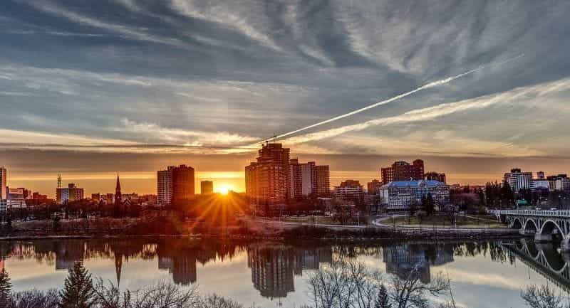 The city of Saskatoon in Saskatchewan, Canada during sunset, featuring several tall buildings and a clear river in front of them.