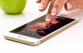 A smartphone lying down flat on a desk with a hand about to tap on its screen.