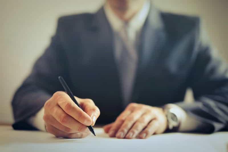 A businessman in a suit signs a deal with a pen.