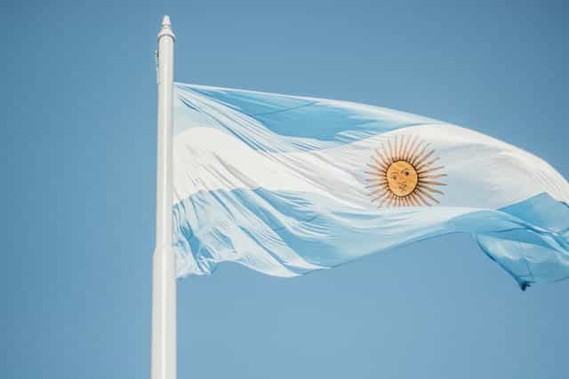 Bendera biru dan putih Argentina melambai di langit biru, di tiang bendera.