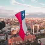 A hand waves the Chilean flag above a big city.