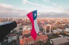 A hand waves the Chilean flag above a big city.
