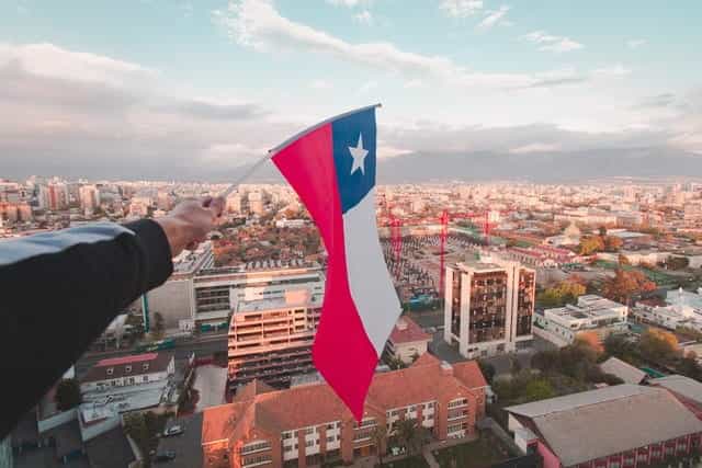 Teks Alt: Sebuah tangan mengibarkan bendera Chili di atas kota besar.