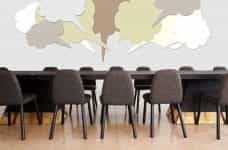A large table in a conference room surrounded by chairs, with many thought bubbles floating above it.