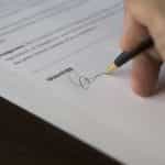 A person’s hand holding a fountain pen signing an important piece of paperwork or a contract.