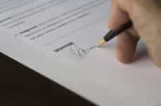 A person’s hand holding a fountain pen signing an important piece of paperwork or a contract.