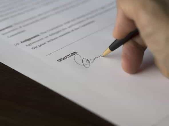 Tangan seseorang yang memegang pulpen menandatangani dokumen penting atau kontrak.