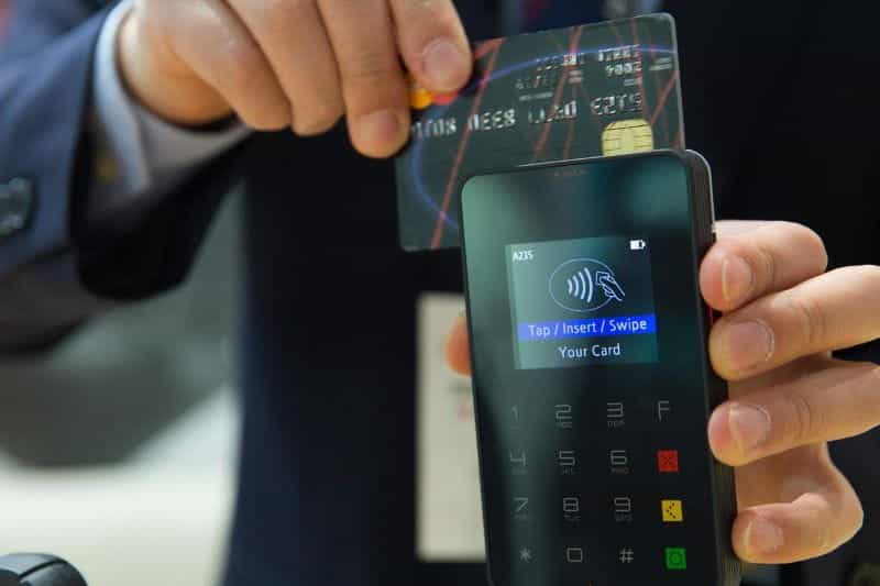 A person swiping their credit card through a card reader terminal, which is displaying a notice for the customer to tap, insert or swipe their card.