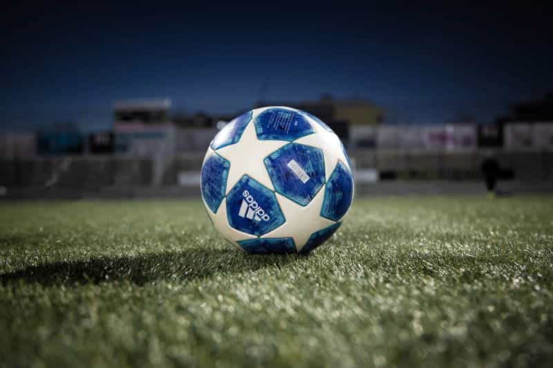 Bola sepak putih dan biru di lapangan rumput hijau di malam hari.