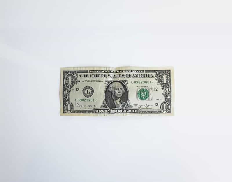 A $1 US bank note sits on a white surface.