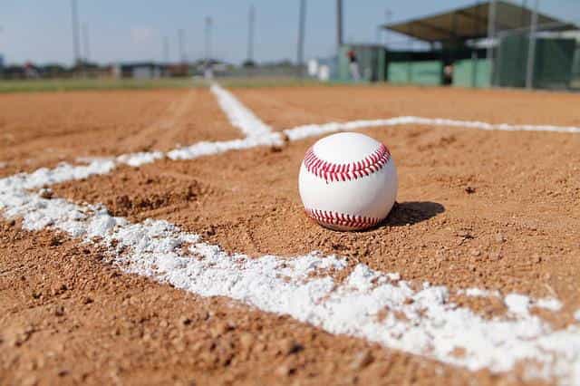 A baseball sitting on the gravel of a baseball pitch/diamond.