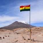 A Bolivian flag waves high up on a flagpole in the desert.