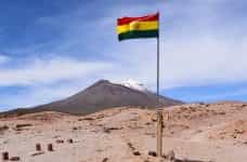 A Bolivian flag waves high up on a flagpole in the desert.