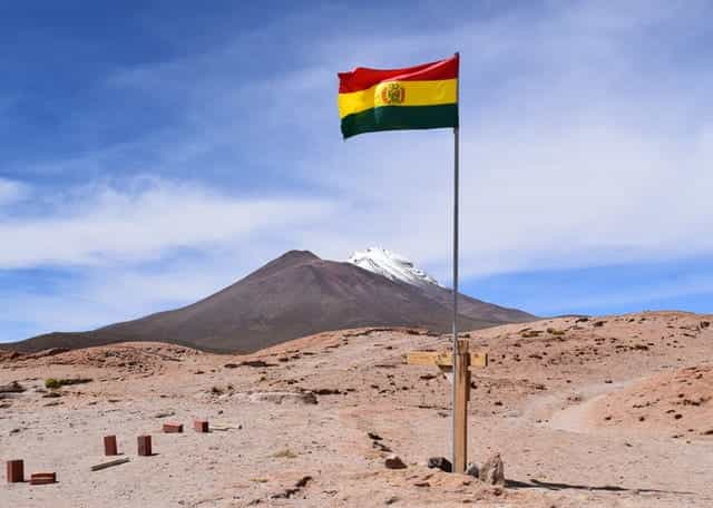 Bendera Bolivia melambai tinggi di tiang bendera di padang pasir.