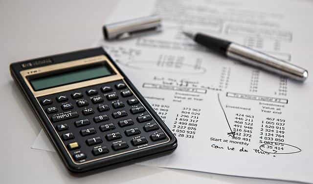 A calculator and fountain pen lying flat on a table on top of paperwork showing the financial performance of a company on it.