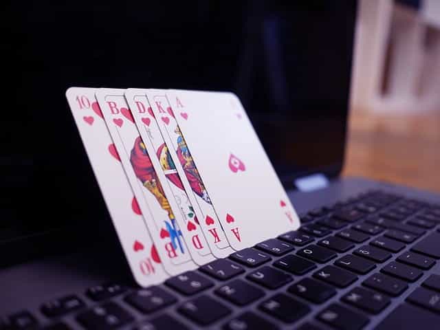 Several playing cards standing in a row and leaning against a laptop computer screen.