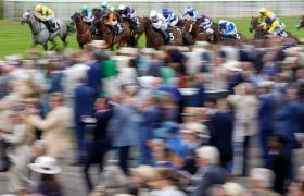 Horses thunder past a packed Goodwood terrace.