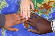 Three hands of people of different races coming together in unity above a map of the Earth.