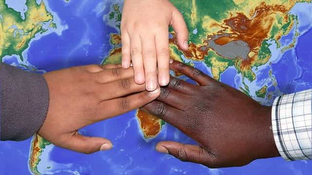 Tiga tangan orang-orang dari ras yang berbeda berkumpul dalam kesatuan di atas peta Bumi.