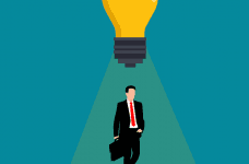 A lightbulb hovering above a man in a suit with a briefcase, shining light down upon him.