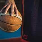 A man in basketball shorts holding a basketball between the tips of his fingers.