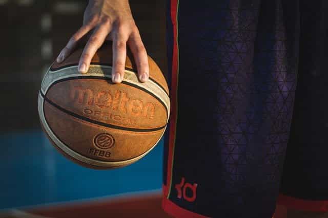 Seorang pria dengan celana pendek basket memegang bola basket di antara ujung jarinya.