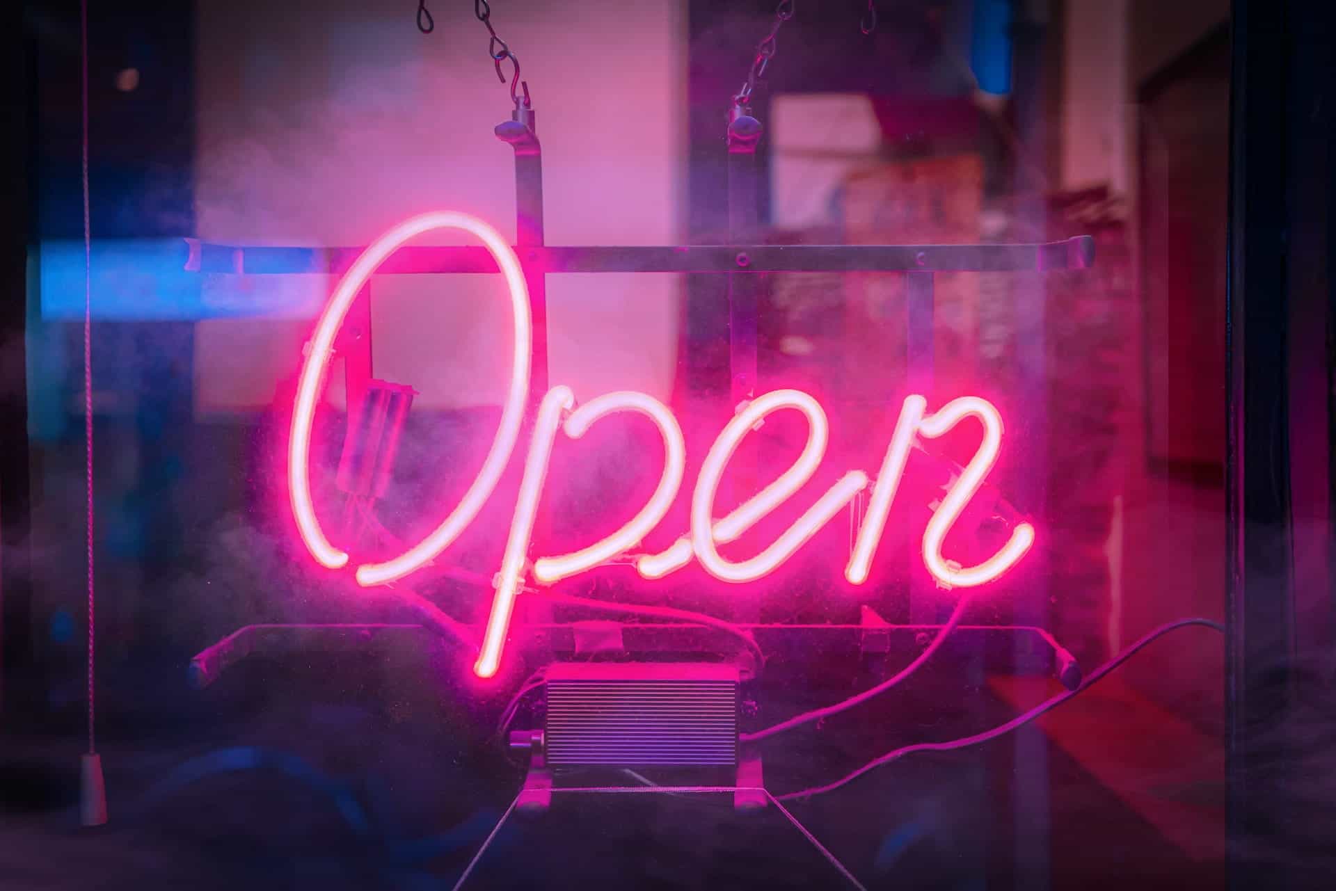 A neon pink light reads "Open" on a glass shop window.