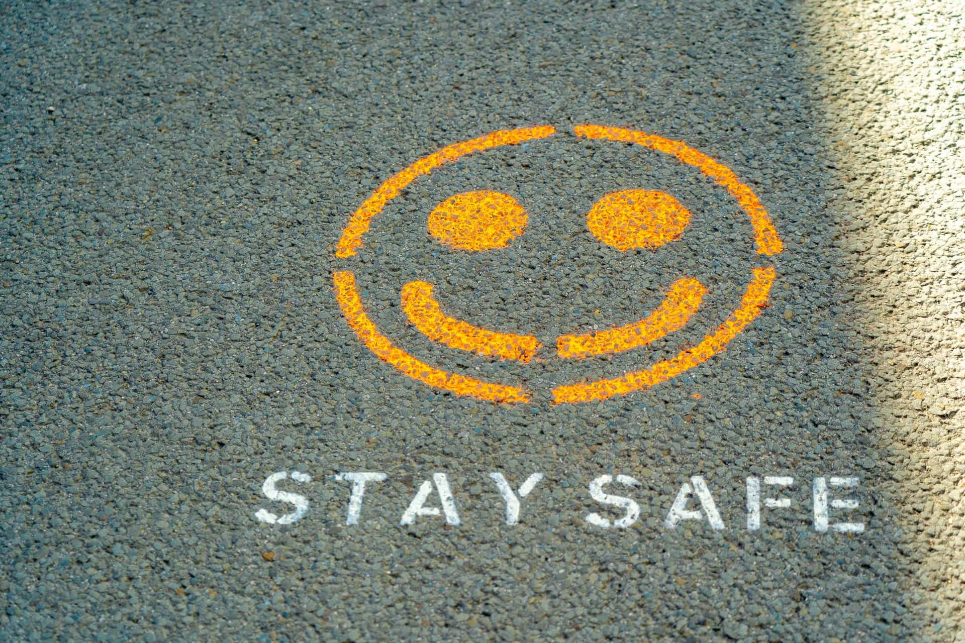 Grafiti oranye di trotoar menunjukkan wajah tersenyum dan teks, TINGGAL AMAN, di bawahnya.