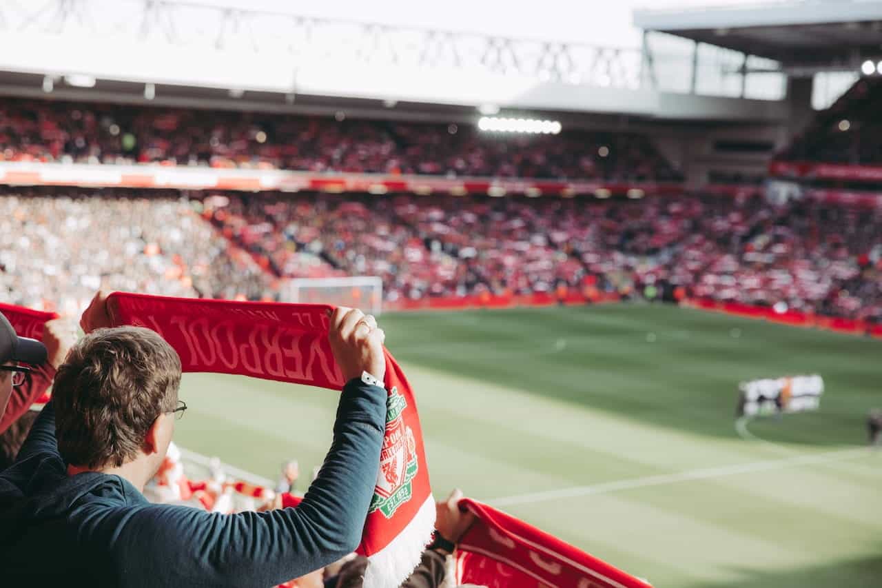 A football fan holding up a Liverpool scarf at a match in a stadium.