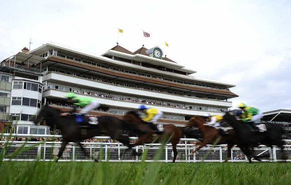 Horses thunder past a packed Newbury Grandstand. 