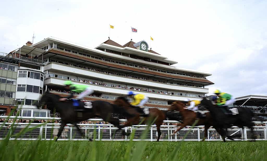 Horses thunder past a packed Newbury Grandstand. 