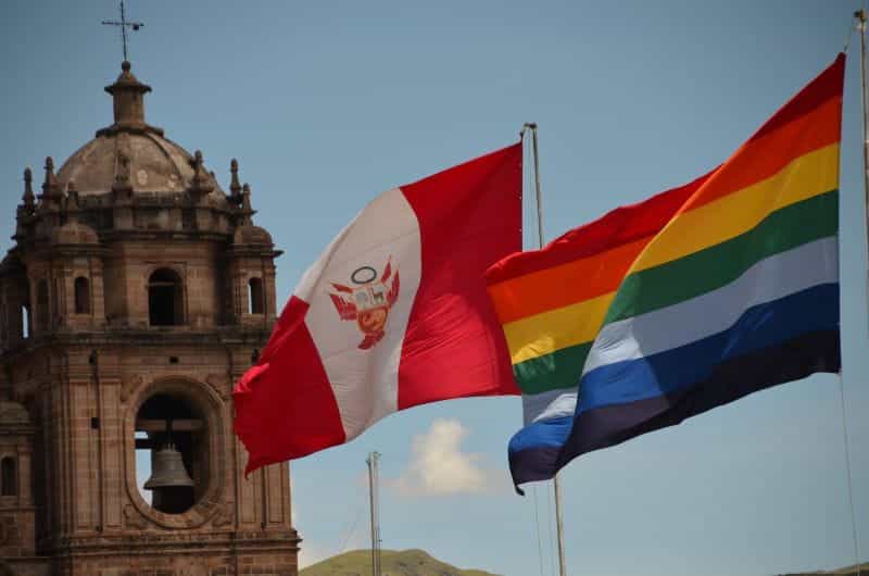 The Peruvian flag waves next to a rainbow flag in Cusco, Peru.