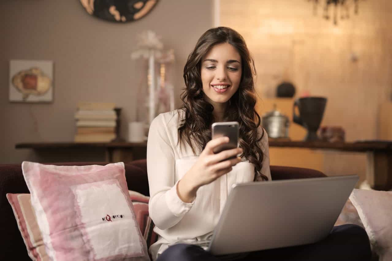 Seorang wanita melihat ponsel dan laptop.