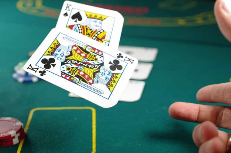 Sebuah tangan melempar dua kartu King ke udara di atas meja atas berwarna hijau di ruang kasino.