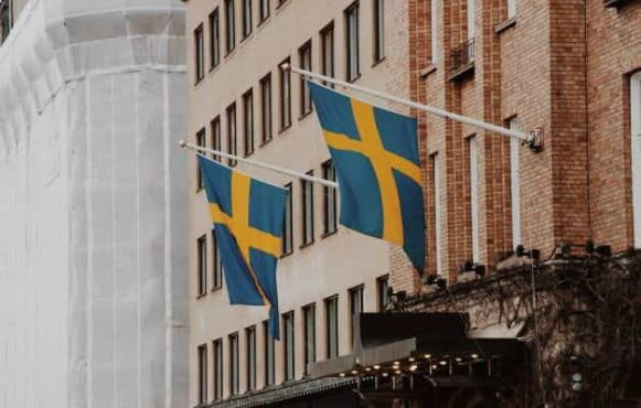 Two Swedish flags hanging at an angle from the front of a building.
