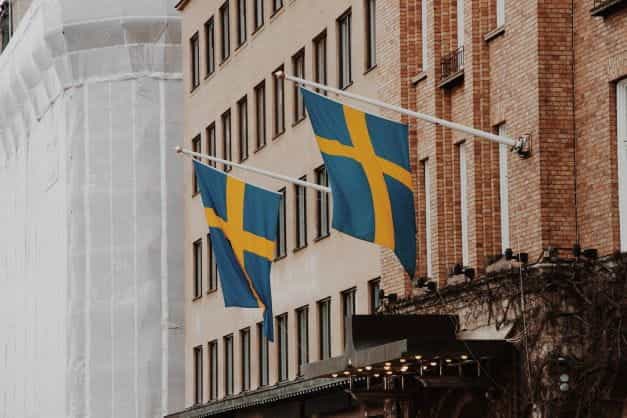 Dua bendera Swedia tergantung di sudut dari depan sebuah bangunan.