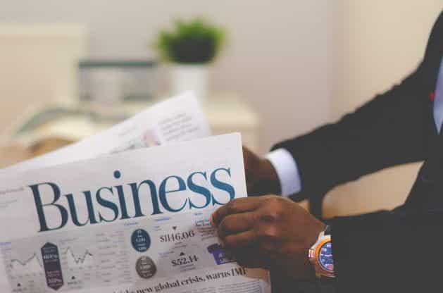 Seorang pria membaca koran bisnis dengan judul terlihat.