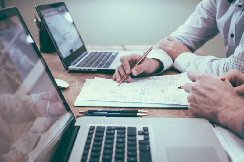 Dua analis keuangan mendiskusikan laporan di meja dengan laptop.