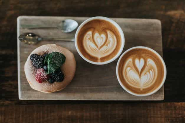 Sebuah puff pastry dan dua cangkir kopi diletakkan di atas nampan saji kayu.