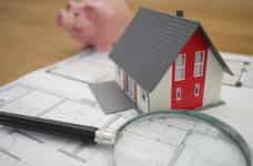 A magnifying glass next to a model of a house and a piggy bank.