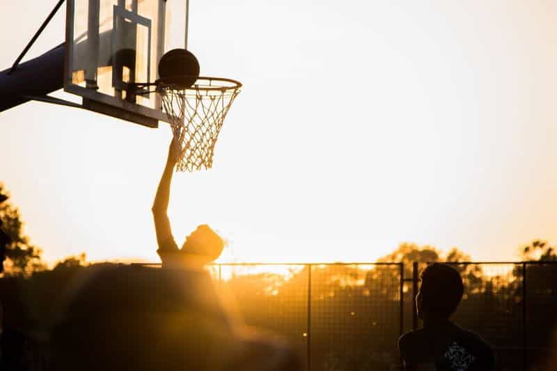 Siluet dua orang bermain basket di luar saat matahari terbenam.