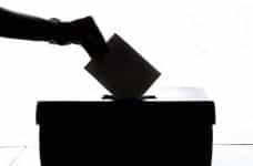 A silhouette of a hand dropping a ballot into a ballot box.