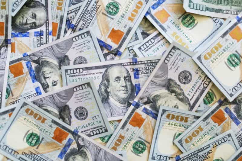 Uang kertas $100 USD menutupi permukaan.
