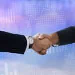 Two peoples’ arms in business suits shaking hands.