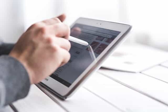 Sebuah tangan memegang stylus dan tablet digital.