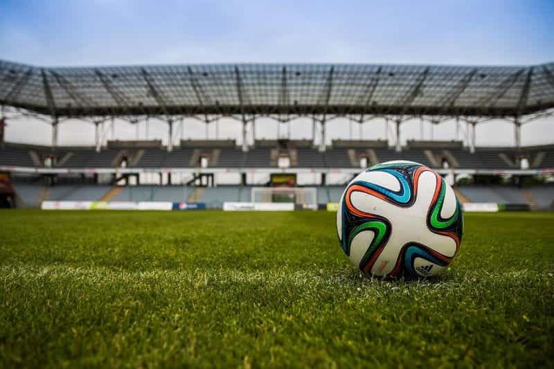 Sebuah bola sepak beristirahat di rumput lapangan sepak bola profesional di stadion besar dan kosong.