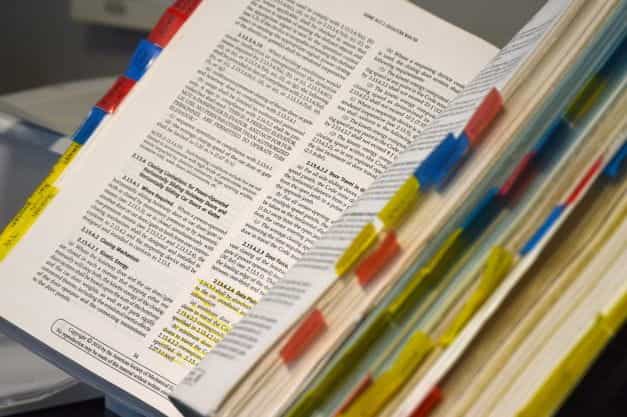 Buku hardbound terbuka dengan anotasi warna-warni di sepanjang tepinya.