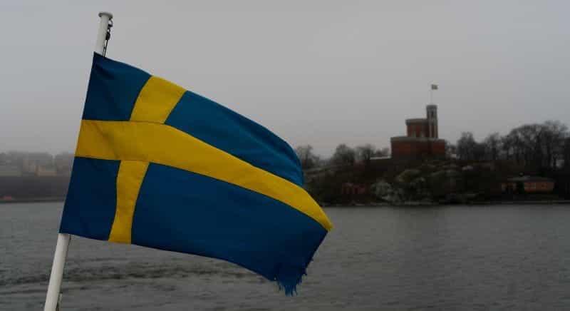 Bendera Swedia dengan sungai dan langit abu-abu di latar belakang.