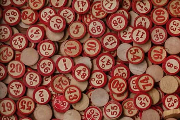 Token bingo kayu bundar yang dicat dengan angka merah tergeletak rata di atas meja.