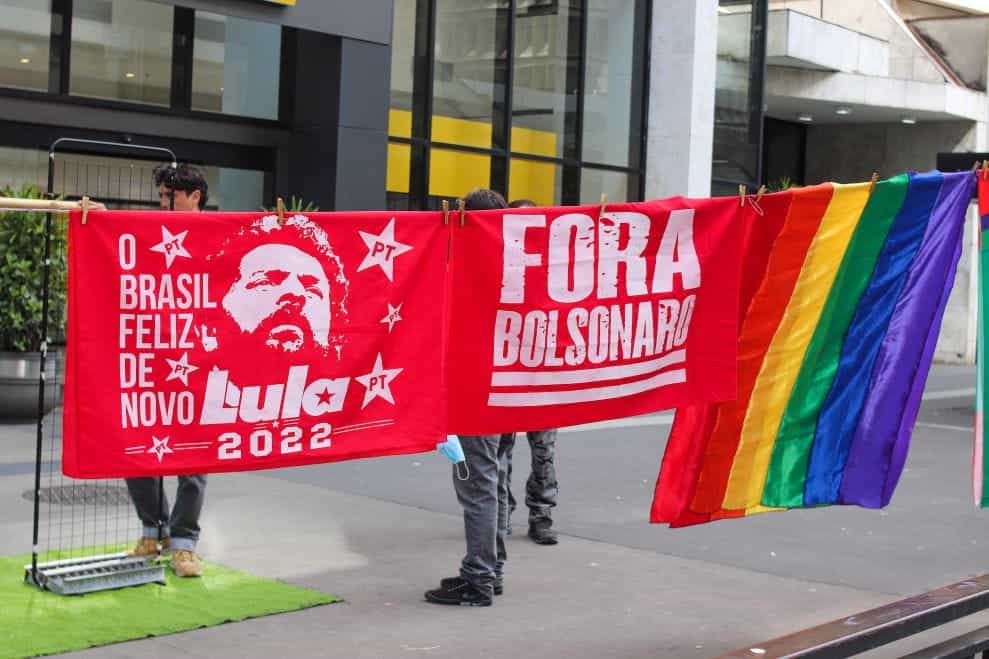 Dua bendera merah menampilkan Lula dan "keluar Bolsonaro" di sebelah bendera pelangi.